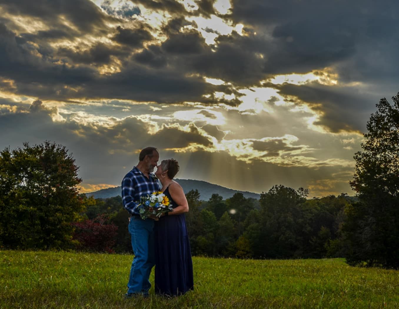 A couple embraces in silhouette against a dramatic sunset sky with mountains in the background.