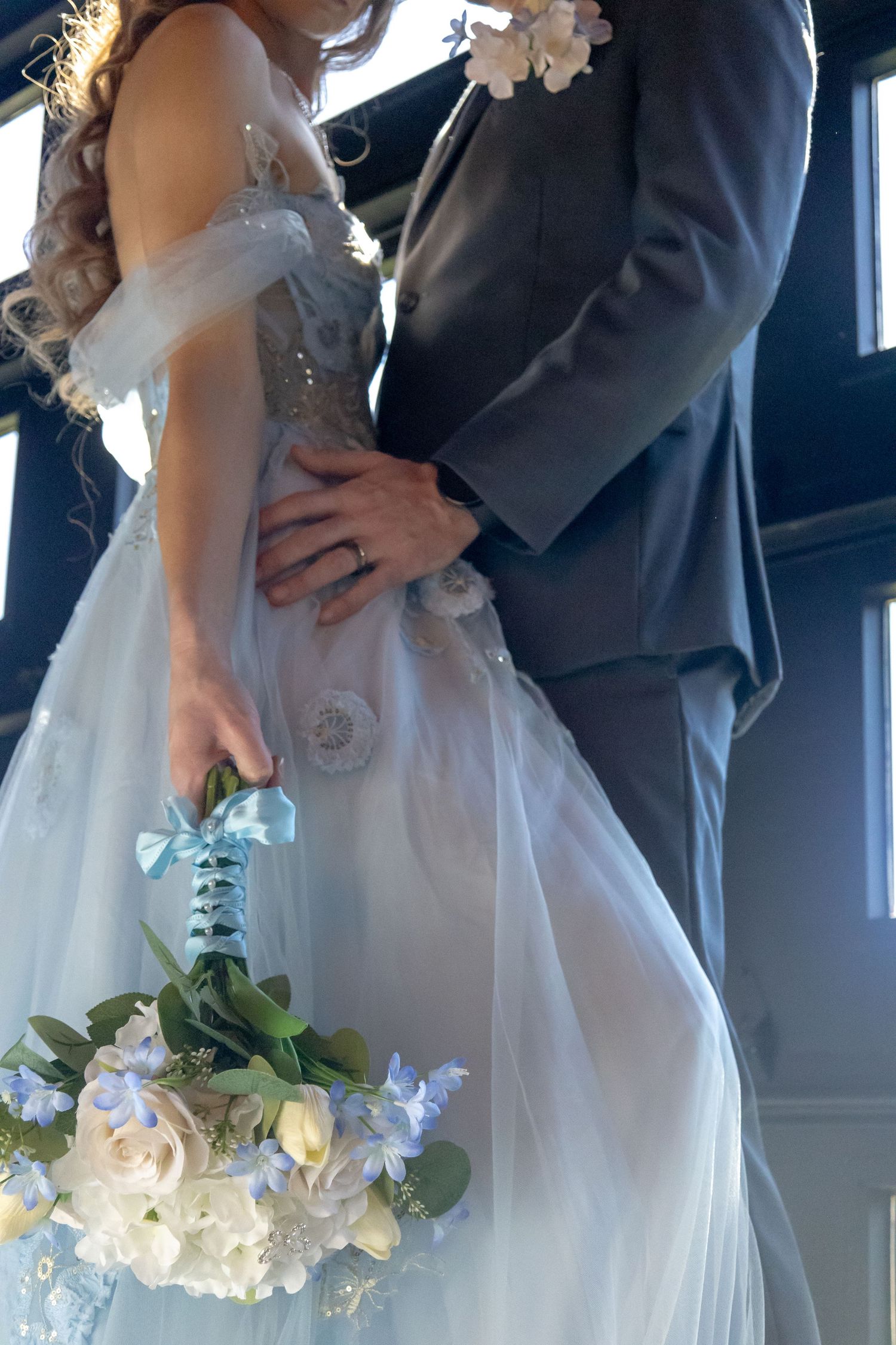 Close-up of a bridal couple holding a white and blue floral bouquet during their wedding ceremony.