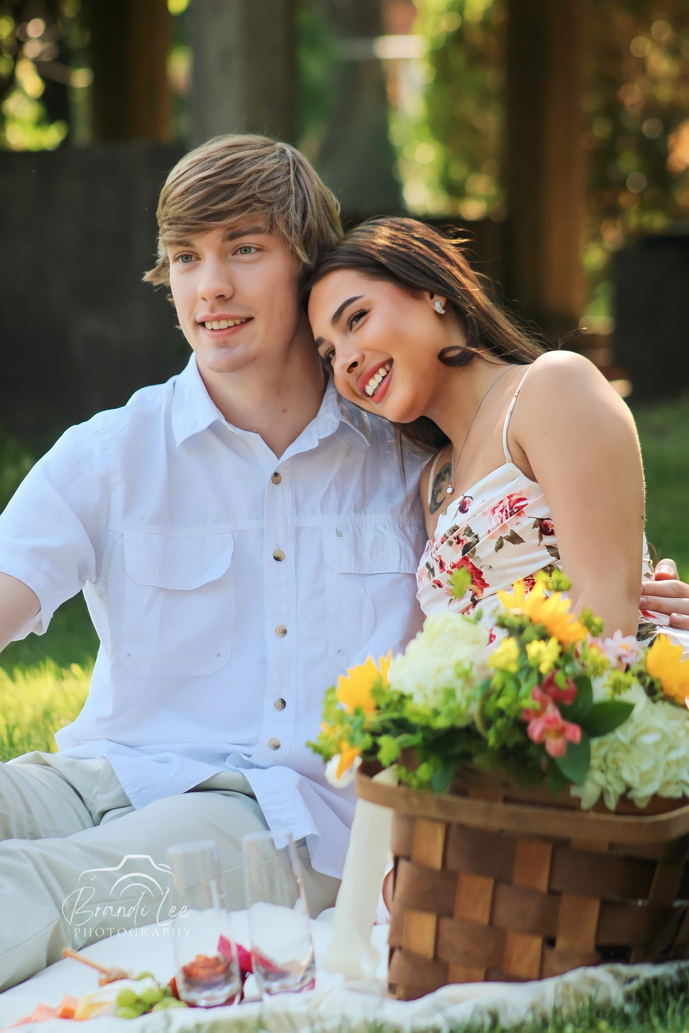 Young couple enjoys romantic picnic with flowers and food basket in sunny garden setting.