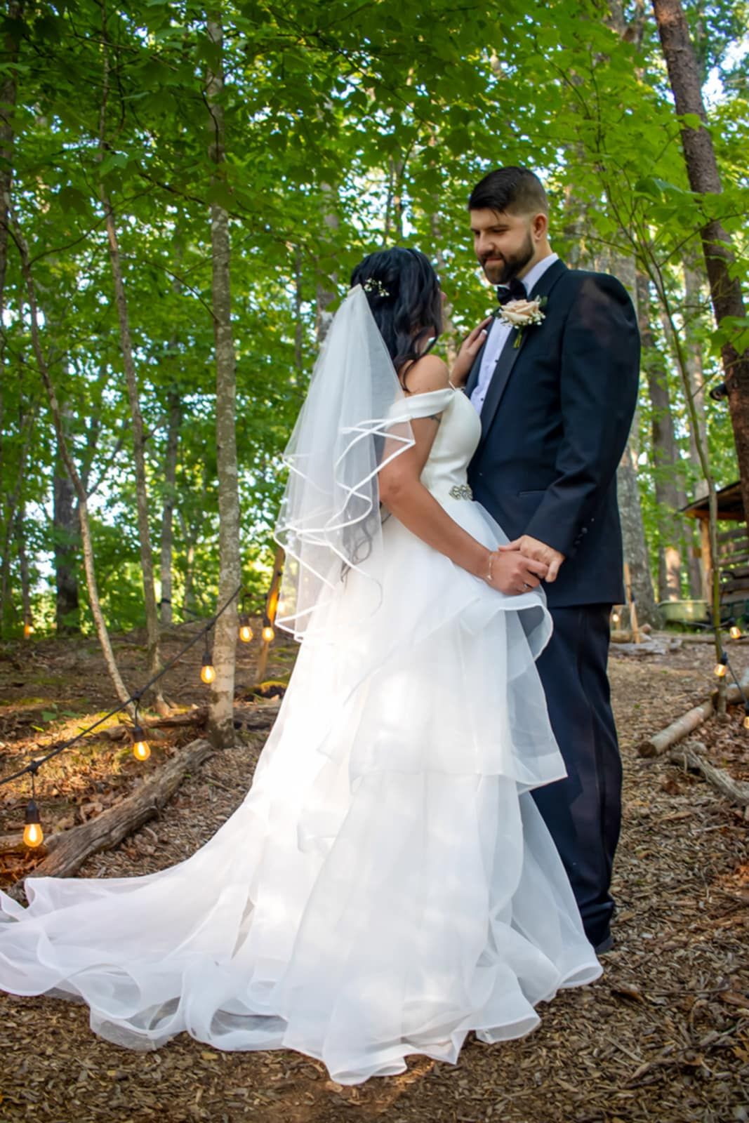 A bride and groom share an intimate moment in a wooded setting, her dress trailing beautifully behind.