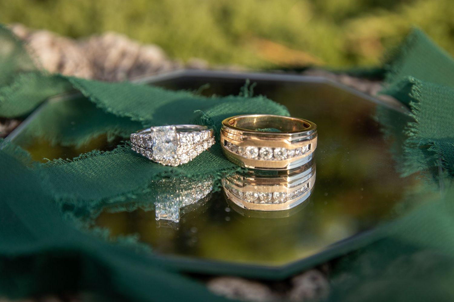 Wedding rings photographed on a green leaf with water droplets creating reflection.