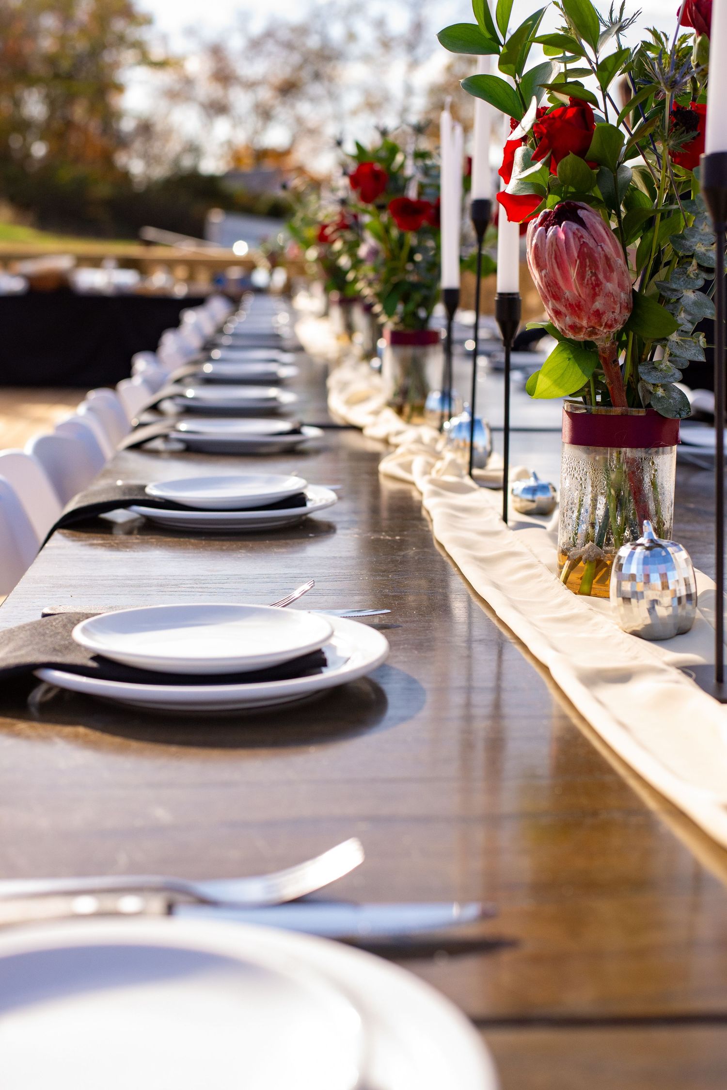 Elegant wedding table setting with white plates and floral centerpieces along a wooden table outdoors.