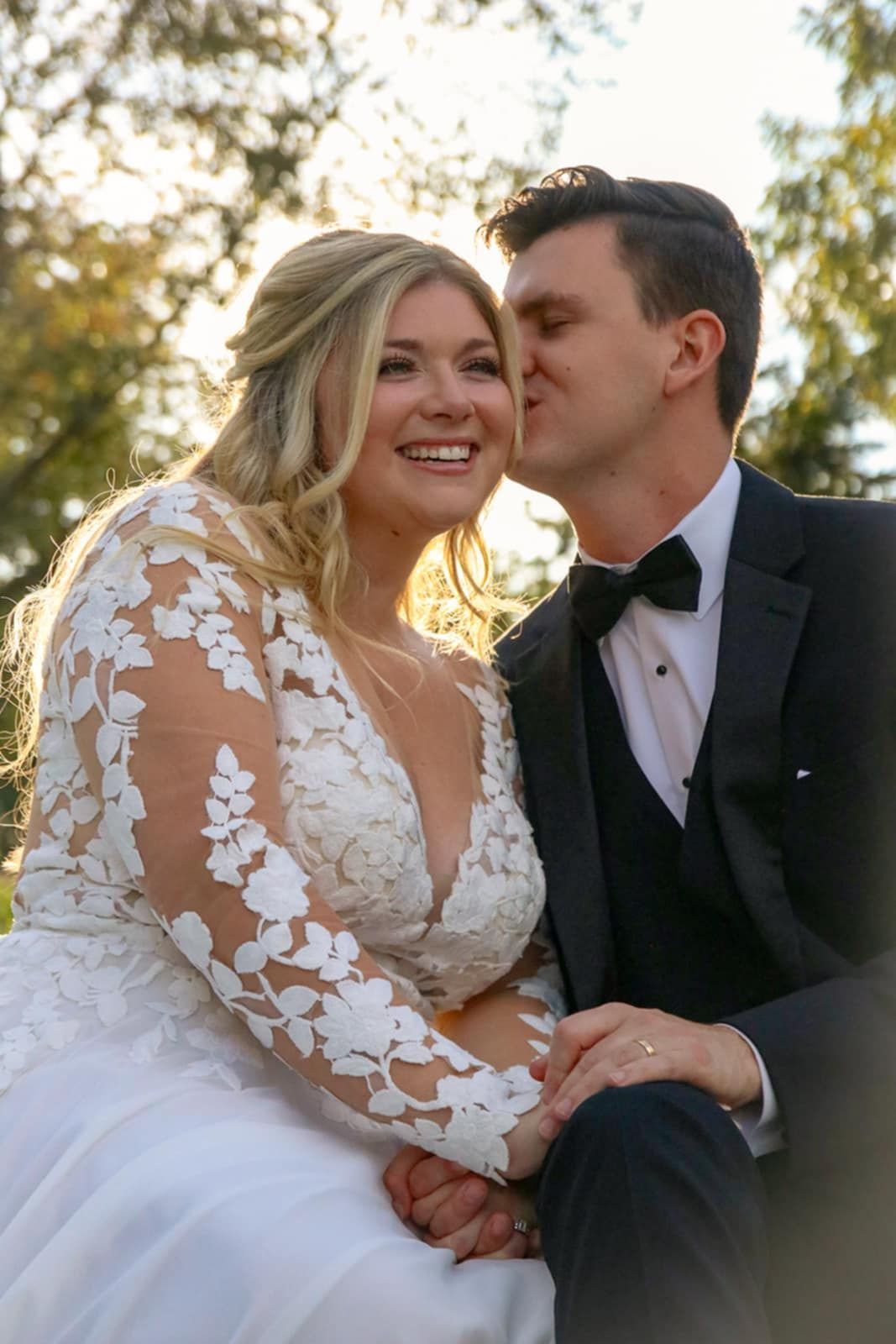 A tender wedding moment captured in warm sunlight with delicate lace details on the dress.