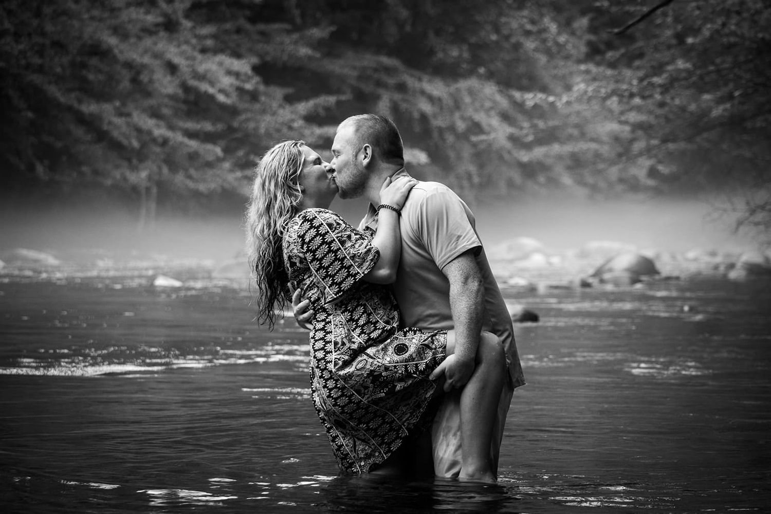 Romantic black and white photo of couple embracing in shallow water.