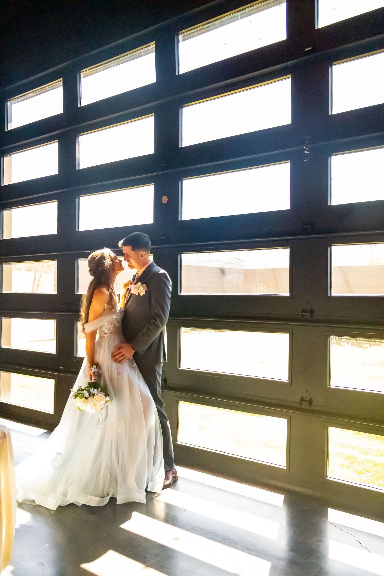 A couple shares an intimate moment in front of a modern glass wall with dramatic backlighting.