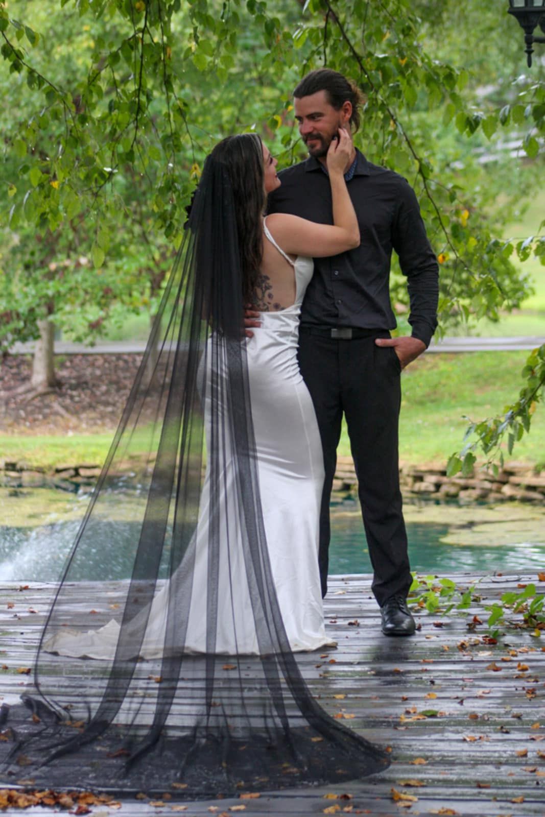 A romantic moment captured on a wooden deck with a dramatic black veil trailing behind.
