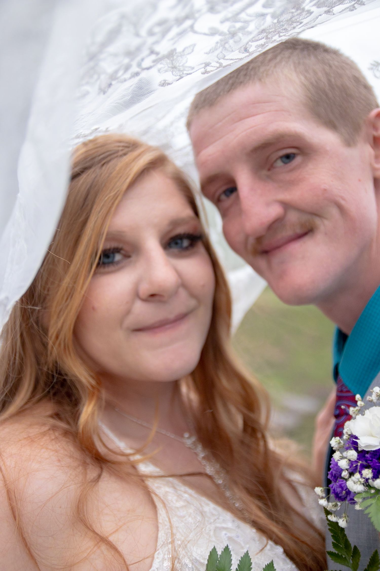 Close-up portrait of a couple on their wedding day with baby's breath flowers and mountains in the background.