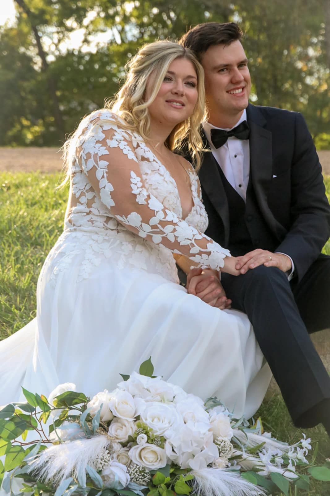 A couple in formal wedding attire sits together with elegant white floral arrangements.