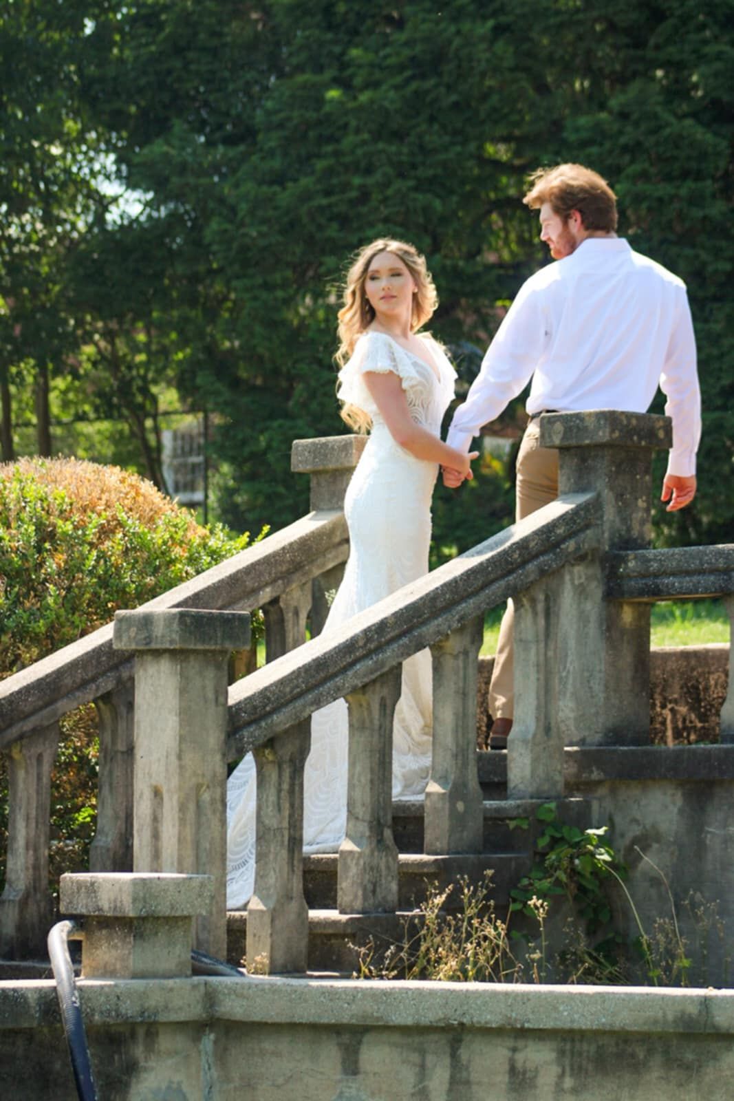 A wedding couple ascending stone steps in an elegant garden setting.