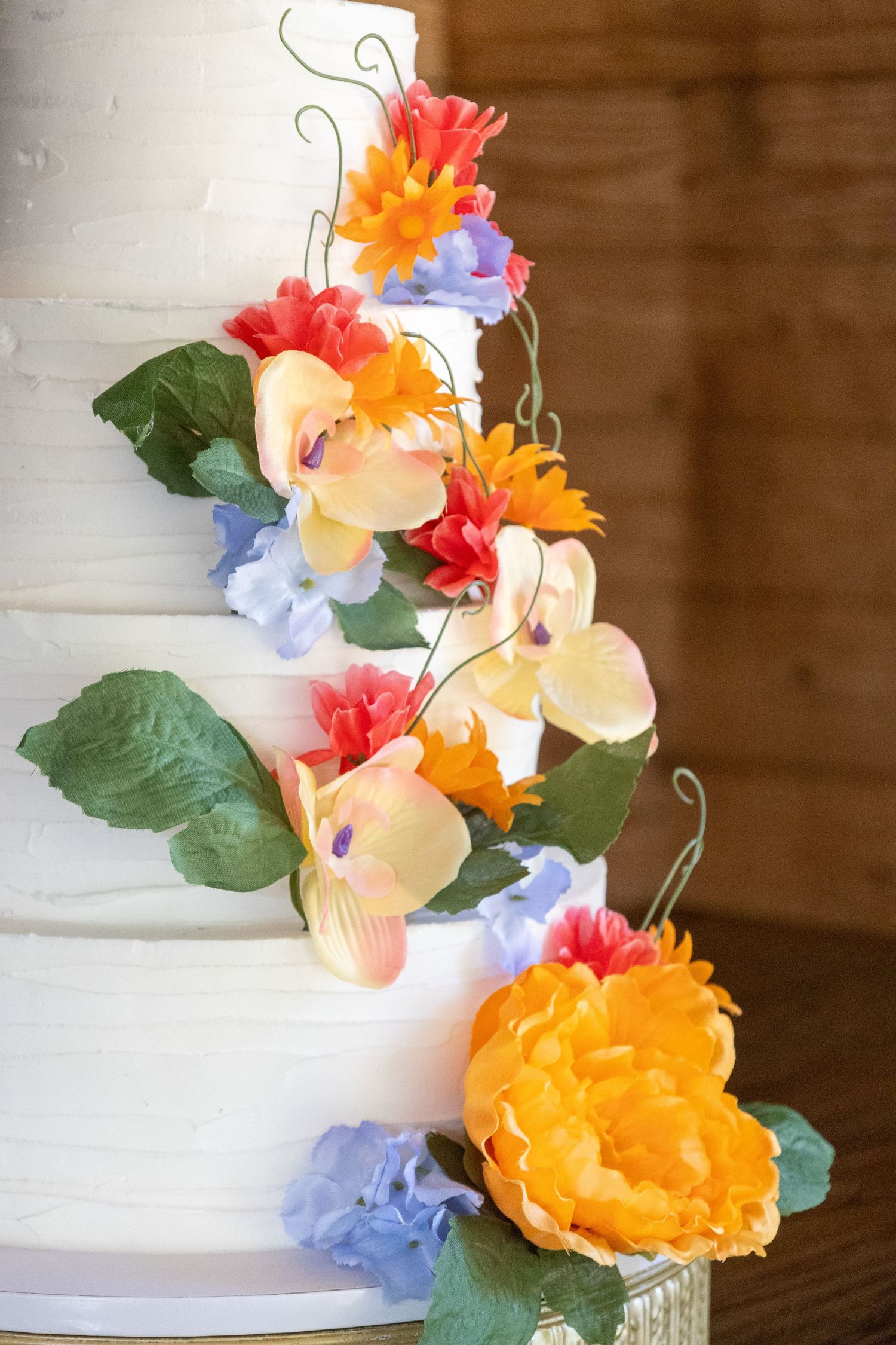 Wedding cake decorated with cascading colorful flowers including orange, pink and blue blooms.