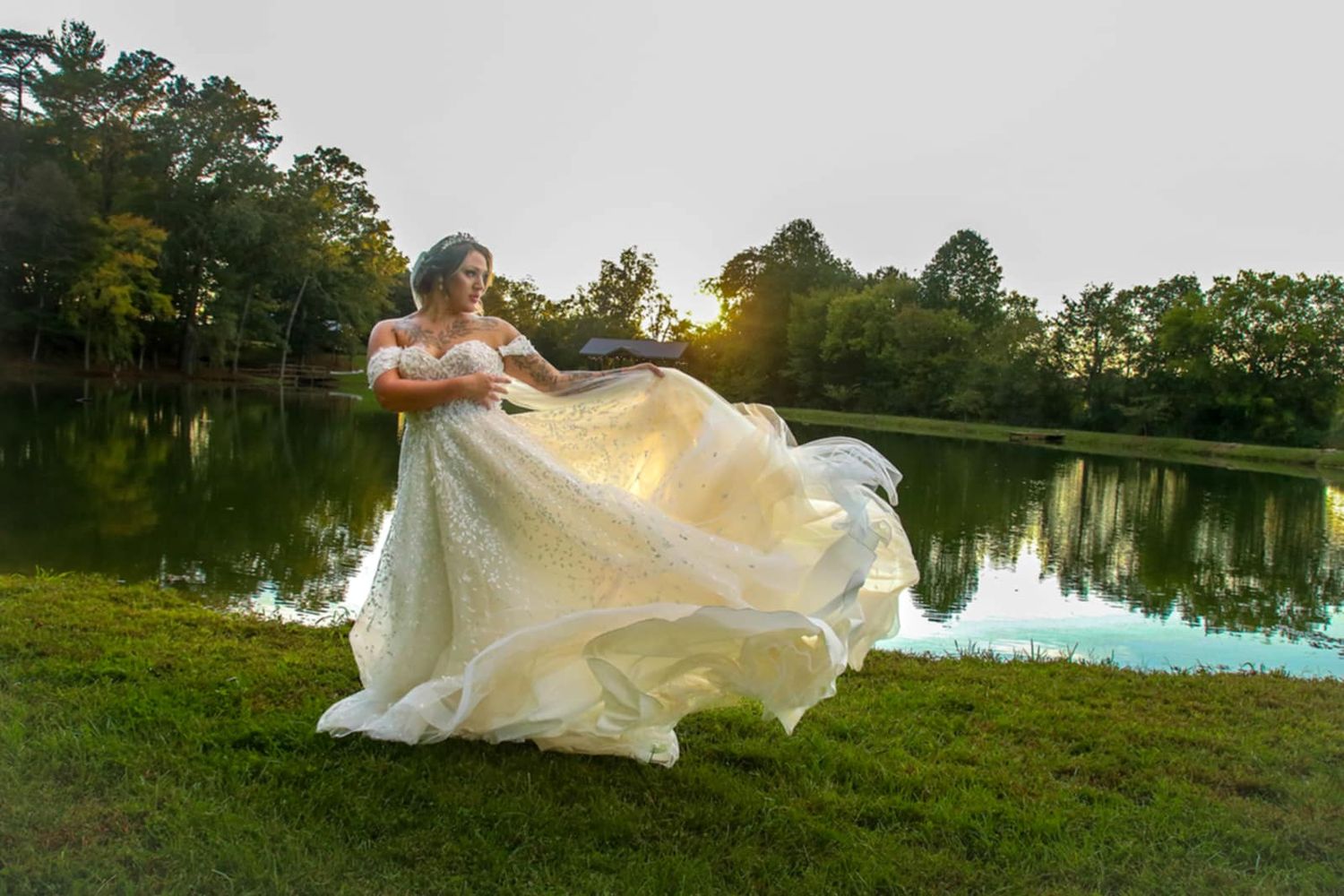 A flowing white wedding dress billows in the breeze against a lakeside backdrop.