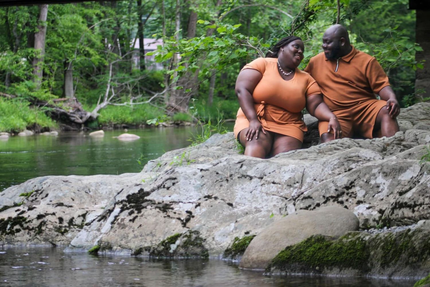 Couple sitting together on large rock formation by peaceful forest stream.