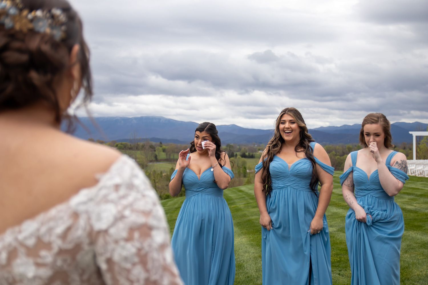 Bridesmaids in matching blue dresses react emotionally to seeing the bride.