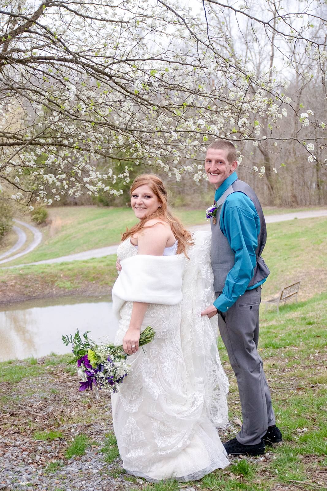 A couple poses together on a spring day with blooming white trees in the background.