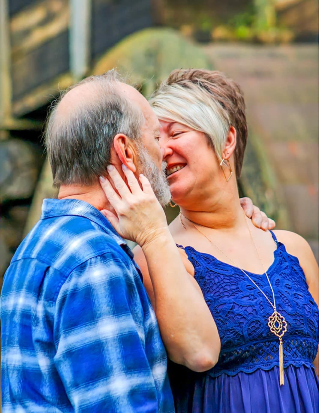 A couple shares an intimate laughing moment while embracing in casual outdoor attire.