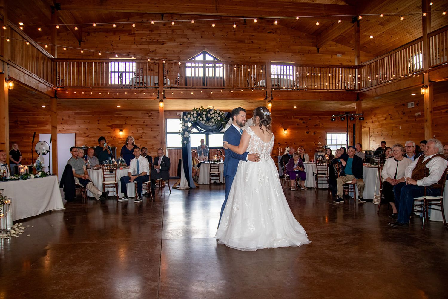 Couple shares their first dance in a rustic wooden reception venue with string lights.