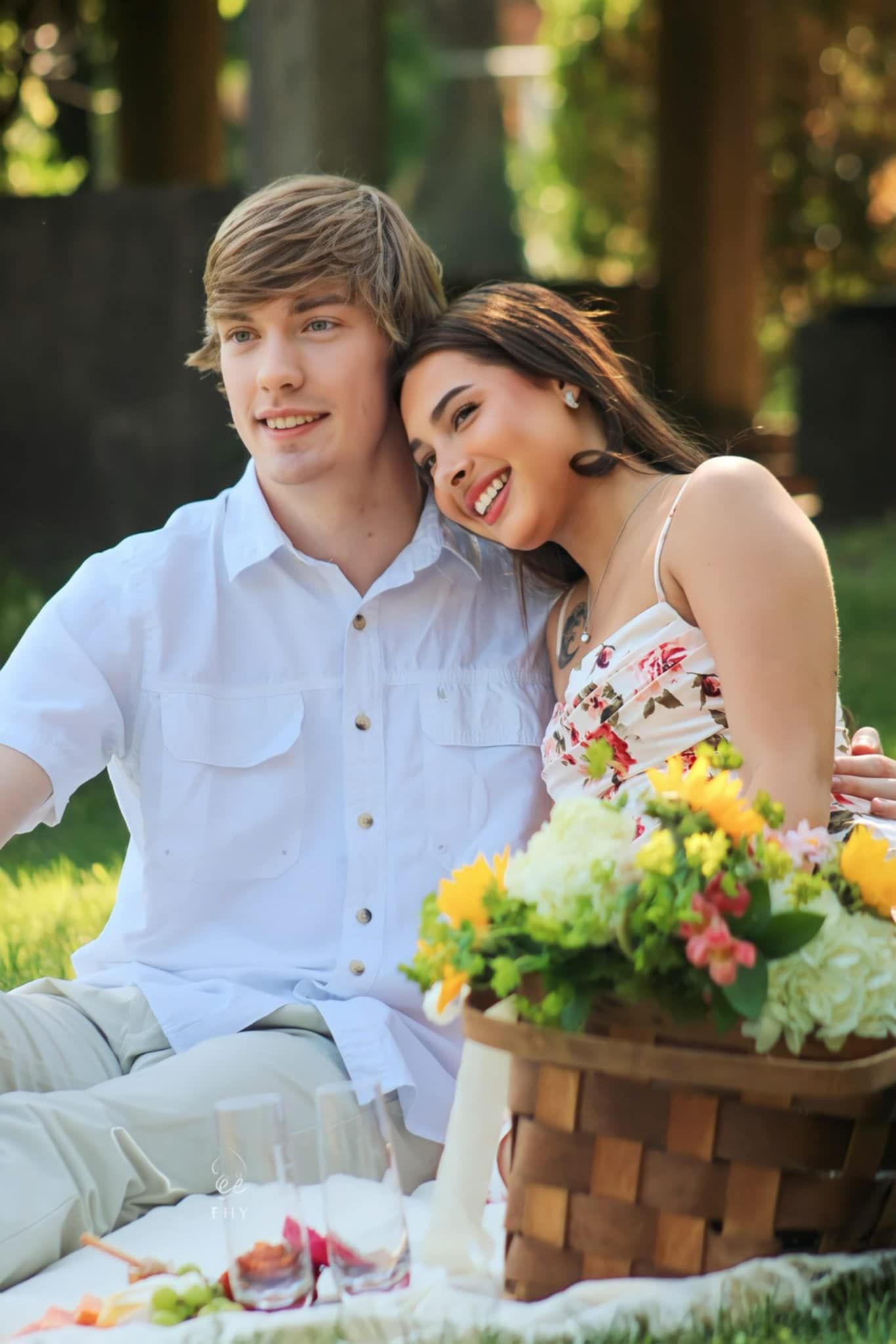 Young couple enjoys romantic picnic with flowers and food basket in sunny garden setting.