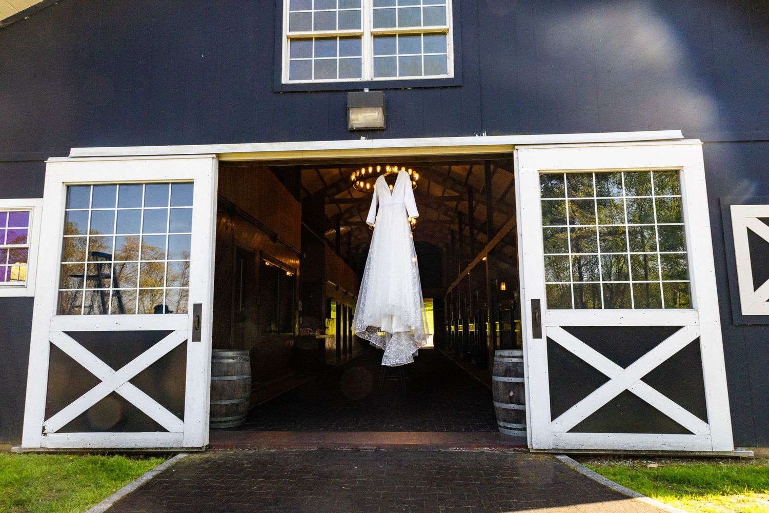 White wedding dress hanging in doorway of navy blue barn with white trim.