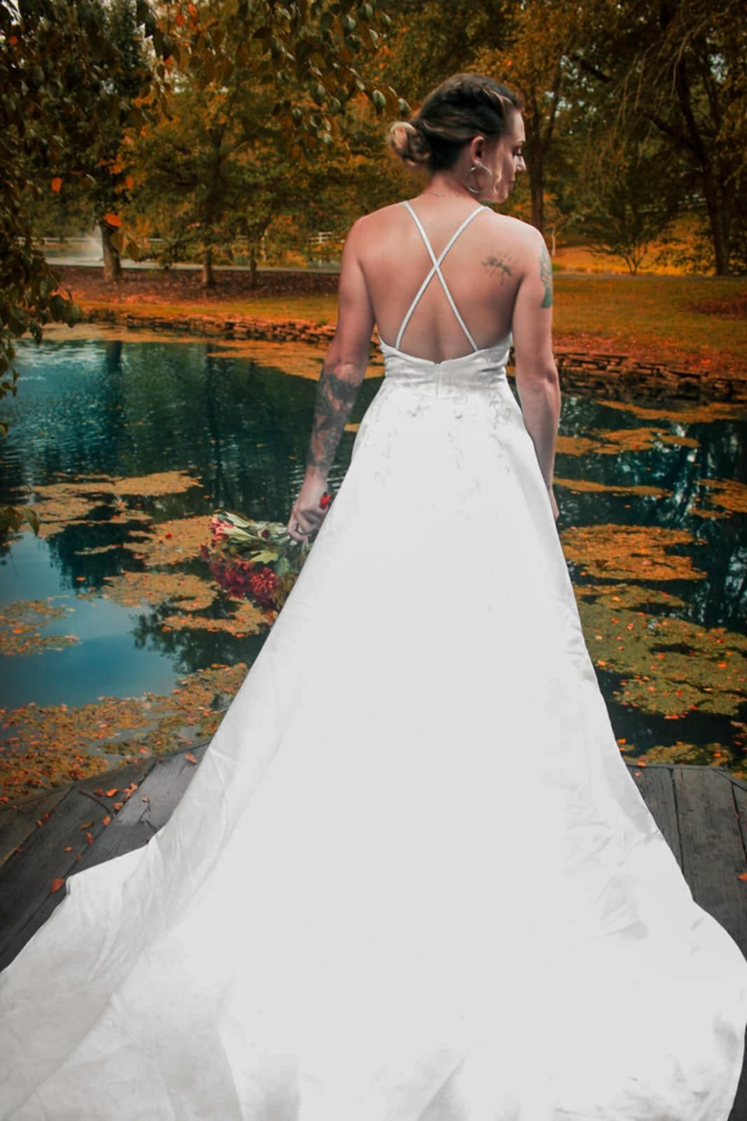 A flowing white wedding dress with cross-back straps photographed near an autumn pond.