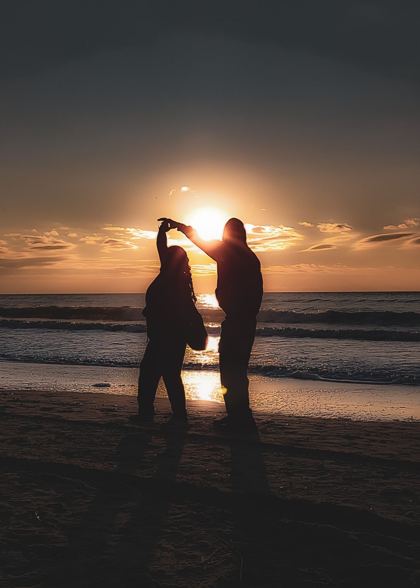 Silhouetted figures stand together on a beach holding hands against a dramatic golden sunset over the ocean.