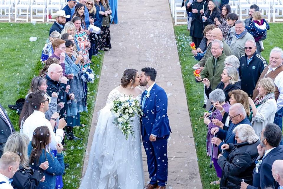 Wedding guests throw confetti as couple walks down outdoor aisle after ceremony.