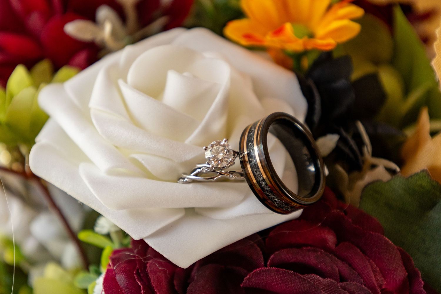 Wedding rings displayed on a white rose surrounded by colorful flowers in a bouquet.