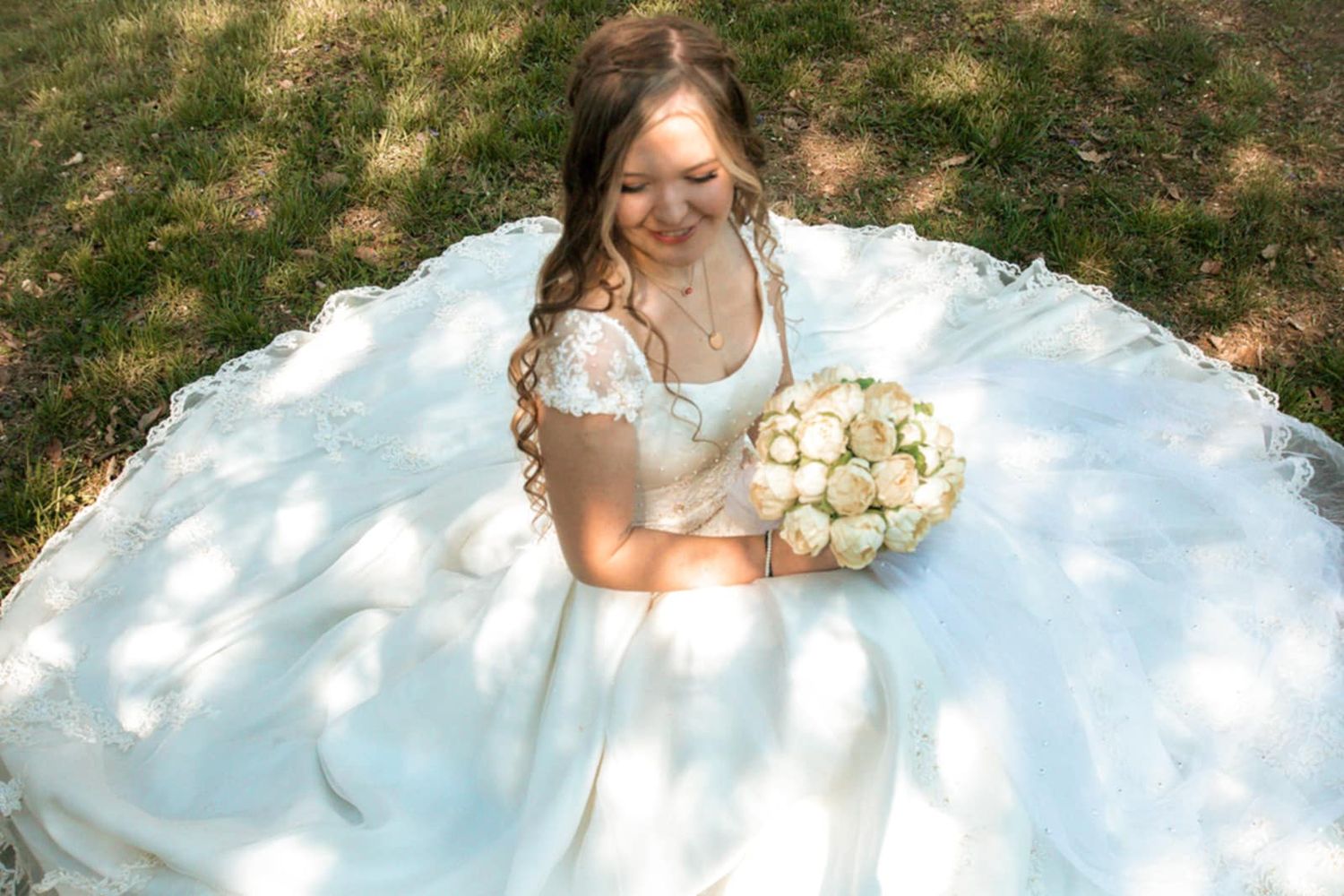 An overhead view of a bride in a white ballgown holding a cream bouquet while seated.