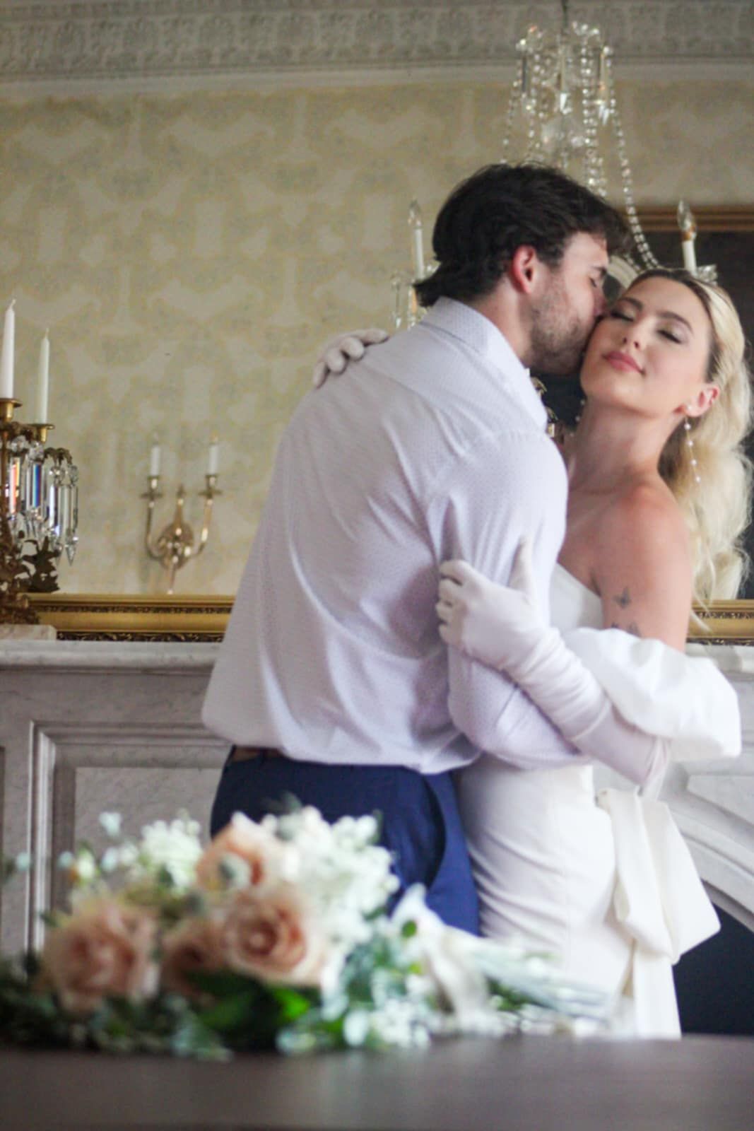 A romantic moment captured in an elegant room with a chandelier and floral arrangements.