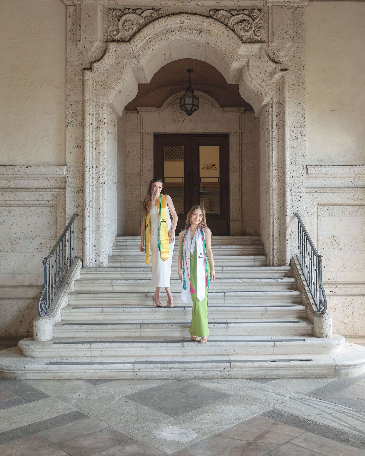Two people stand on an elegant marble staircase with ornate architectural details and iron railings in a historic building at UT