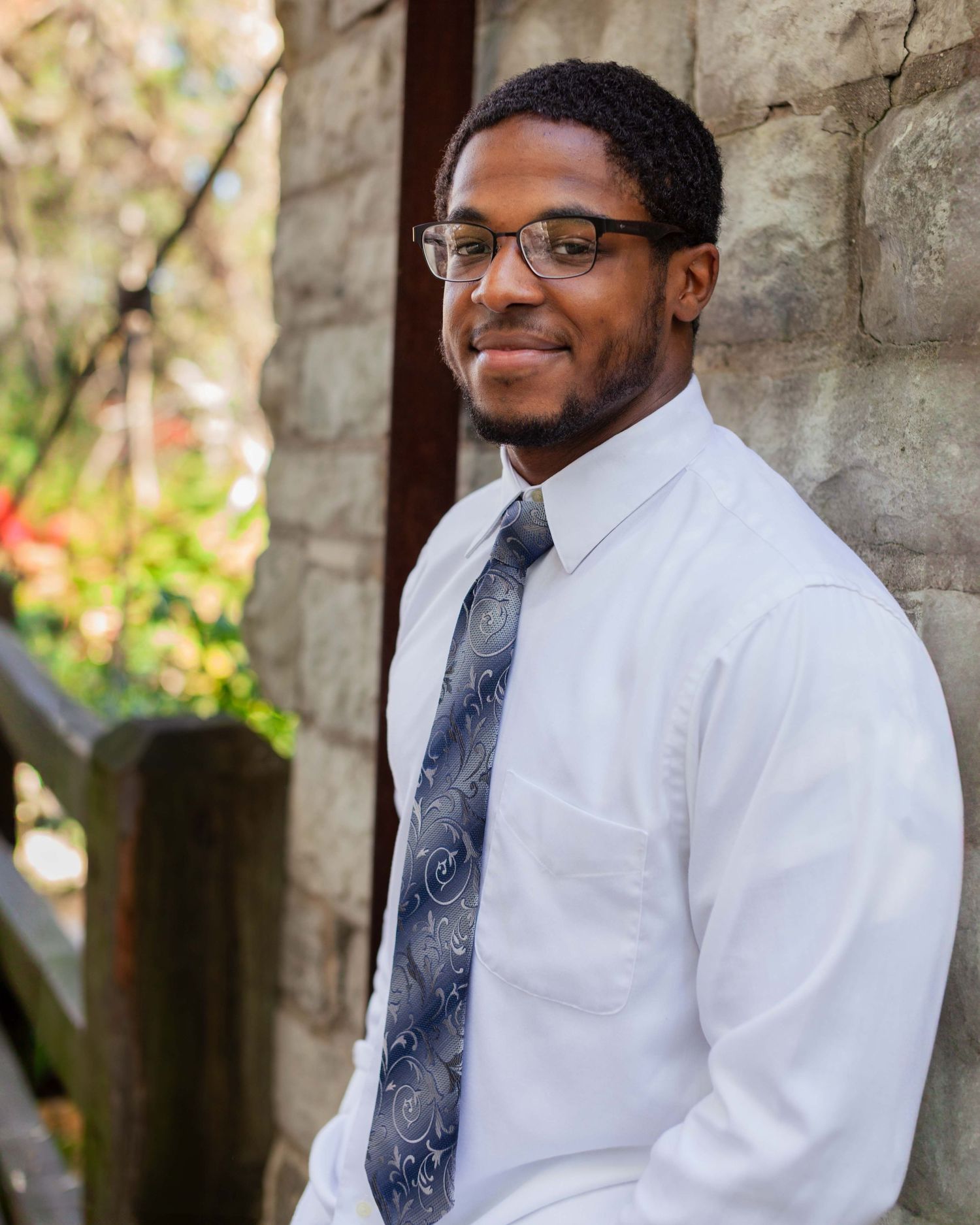 Senior Portrait shot underneath stone arches showing warm smile in white dress shirt and patterned tie.