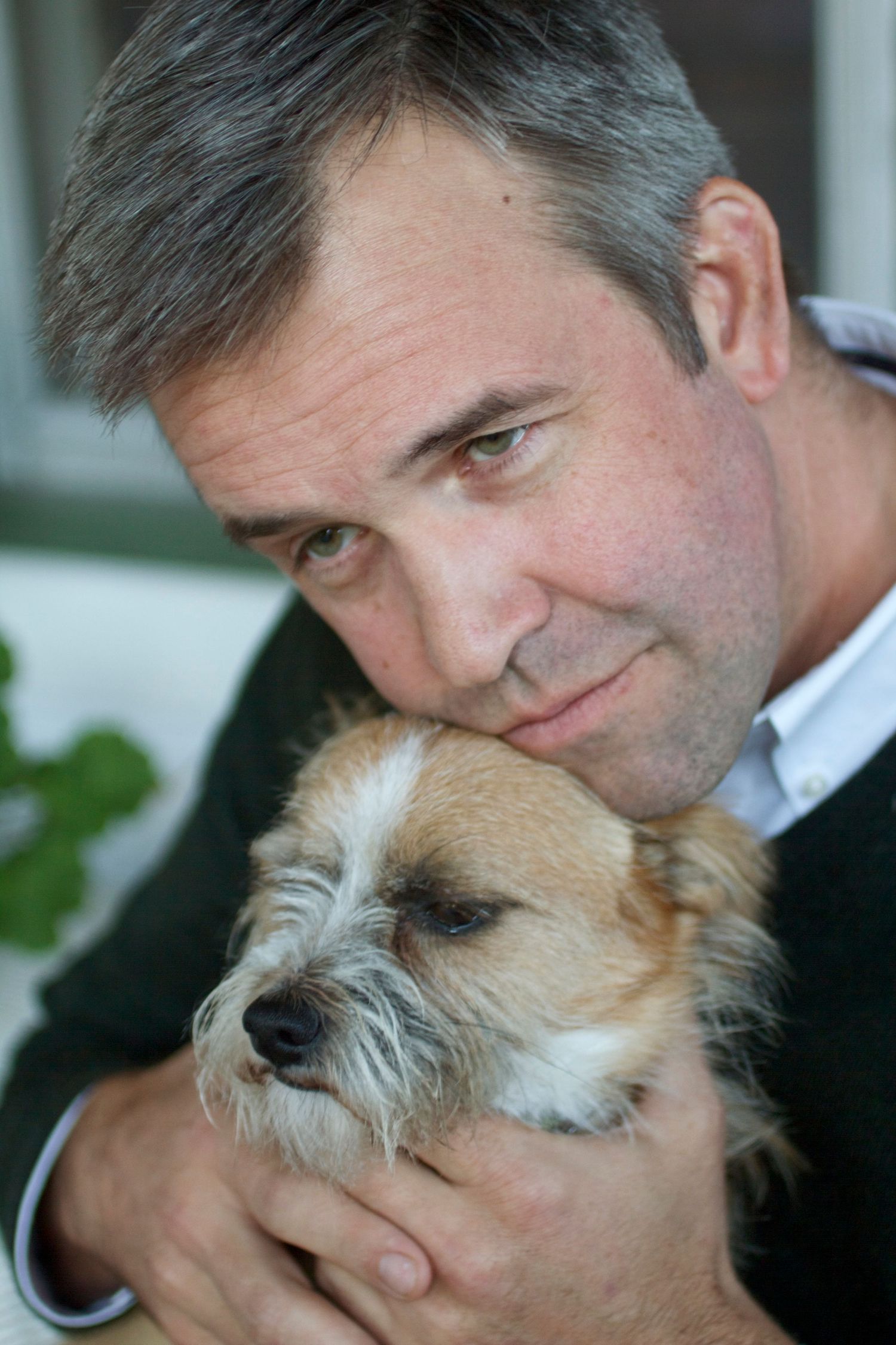 A Hooman man lovingly holds a scruffy tan and white terrier mix dog close to his face.