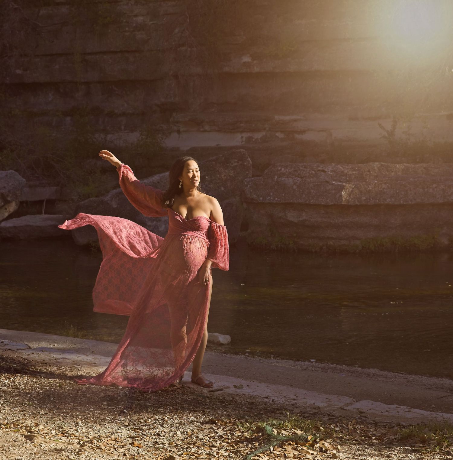 A dancer in a flowing pink dress poses gracefully against dramatic lighting and a stone backdrop.