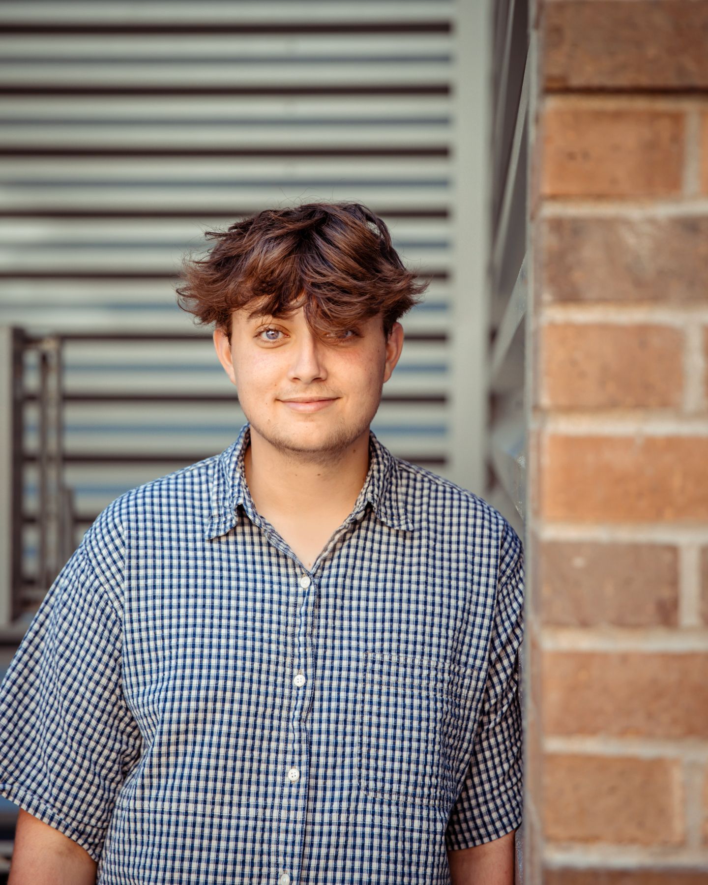 A handsome senior leans up against a brick wall and smiles.