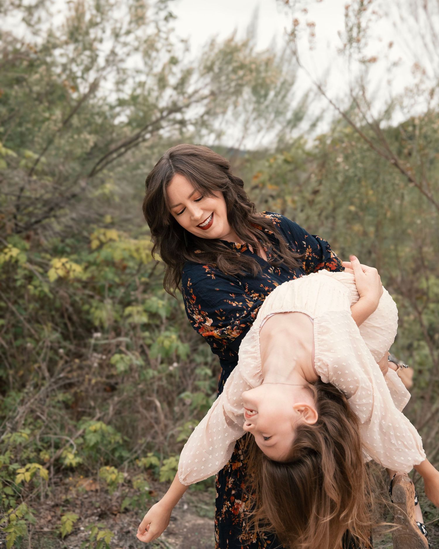 Mom holds her daughter and let's fall back in her arms in a natural backdrop.