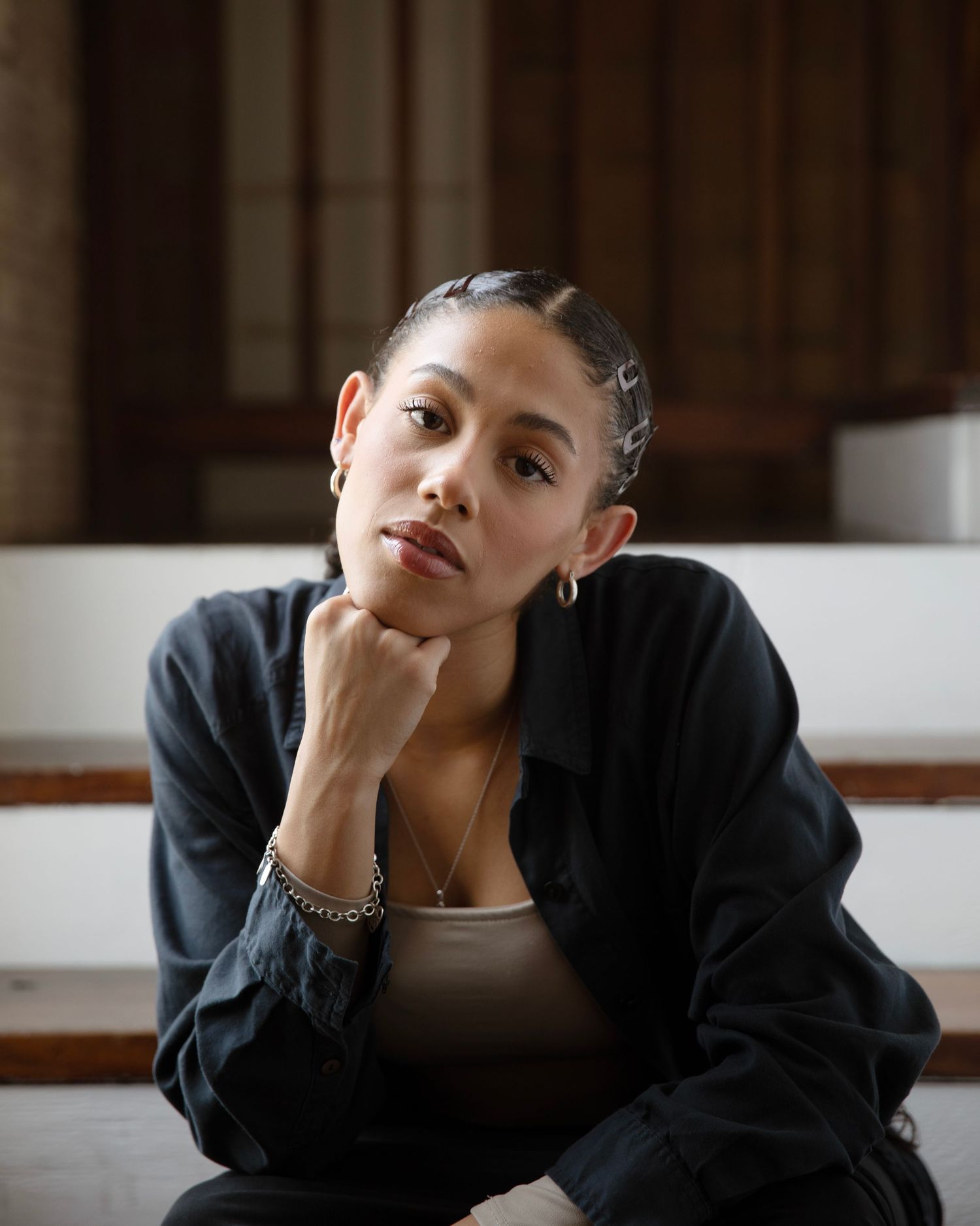 Senior Portrait of girl with braided hair wearing black cardigan and beige top sitting thoughtfully.