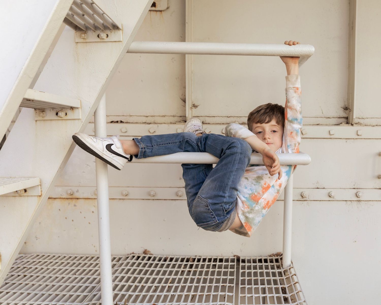 A young boy in jeans climbs and hangs playfully from white metal bars in an urban setting downtown, Austin.