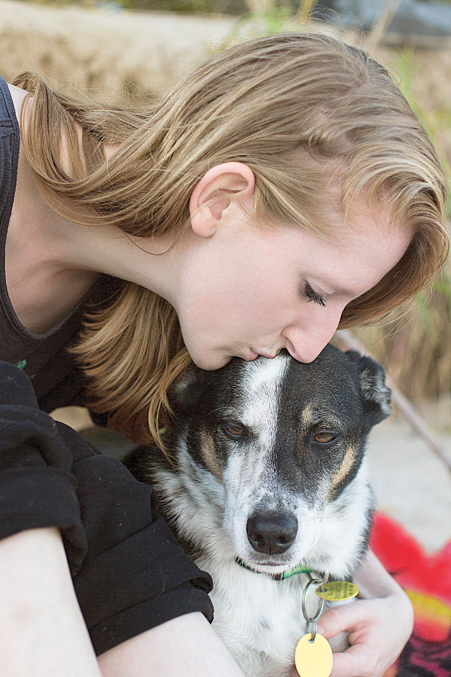 A loving moment between a person with blonde hair and their black and white dog as they share a gentle embrace.