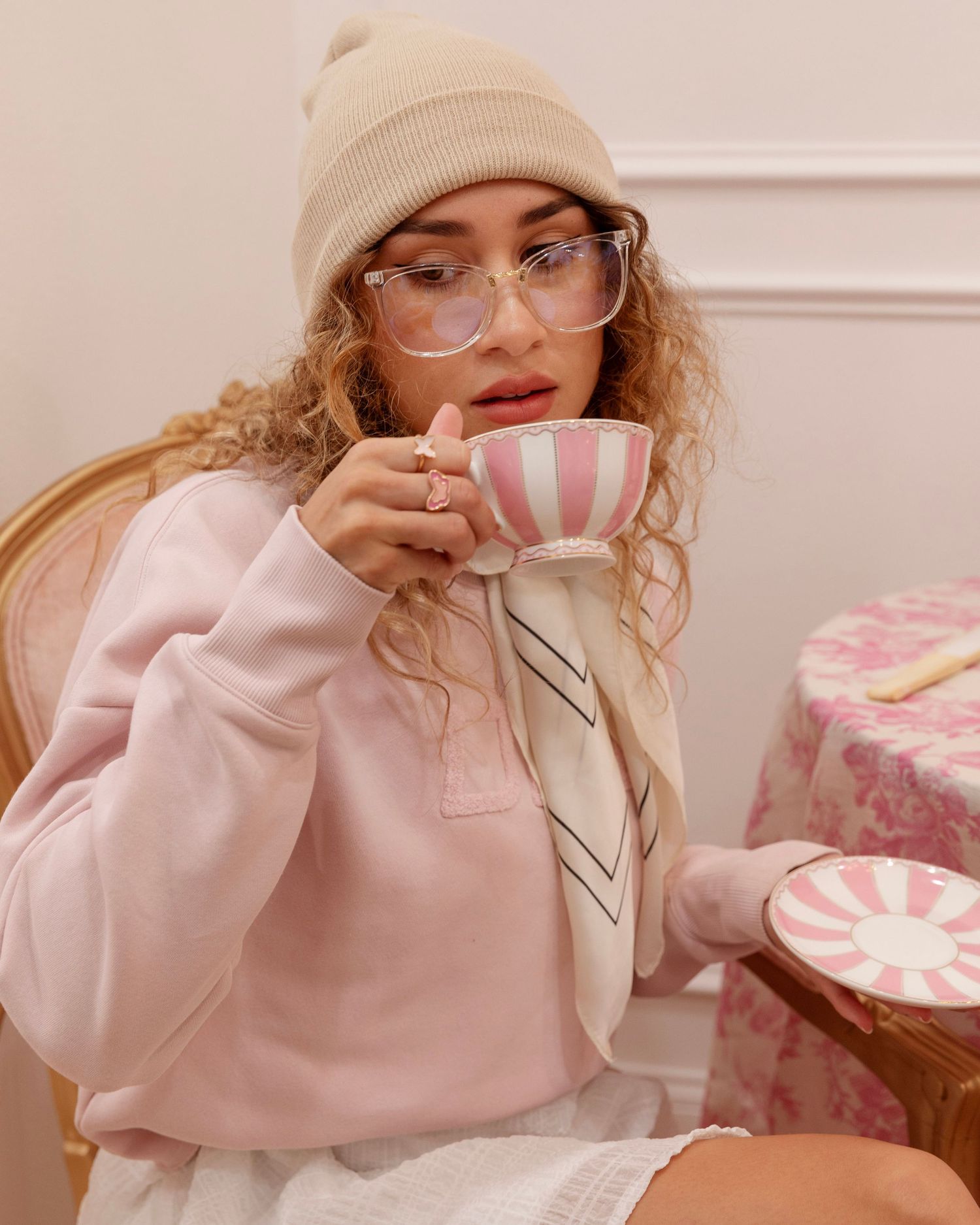 An attractive model dressed in pick, drinks tea from a pink tea cup.