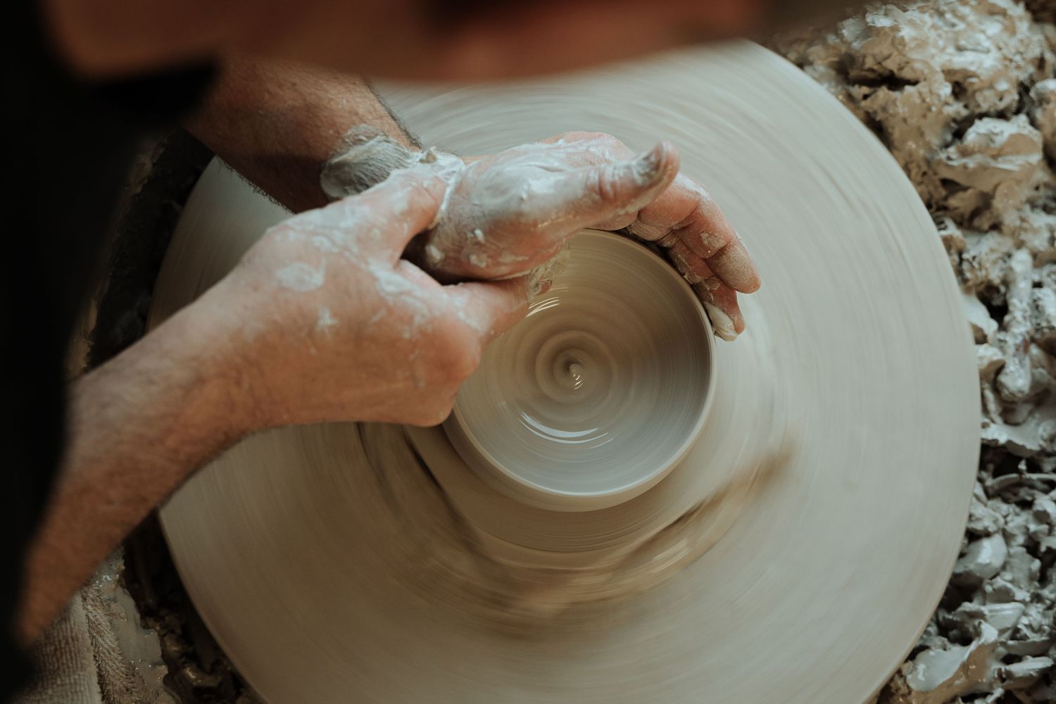 Overhead view of hands shaping a spinning clay bowl on a pottery wheel with slip.
