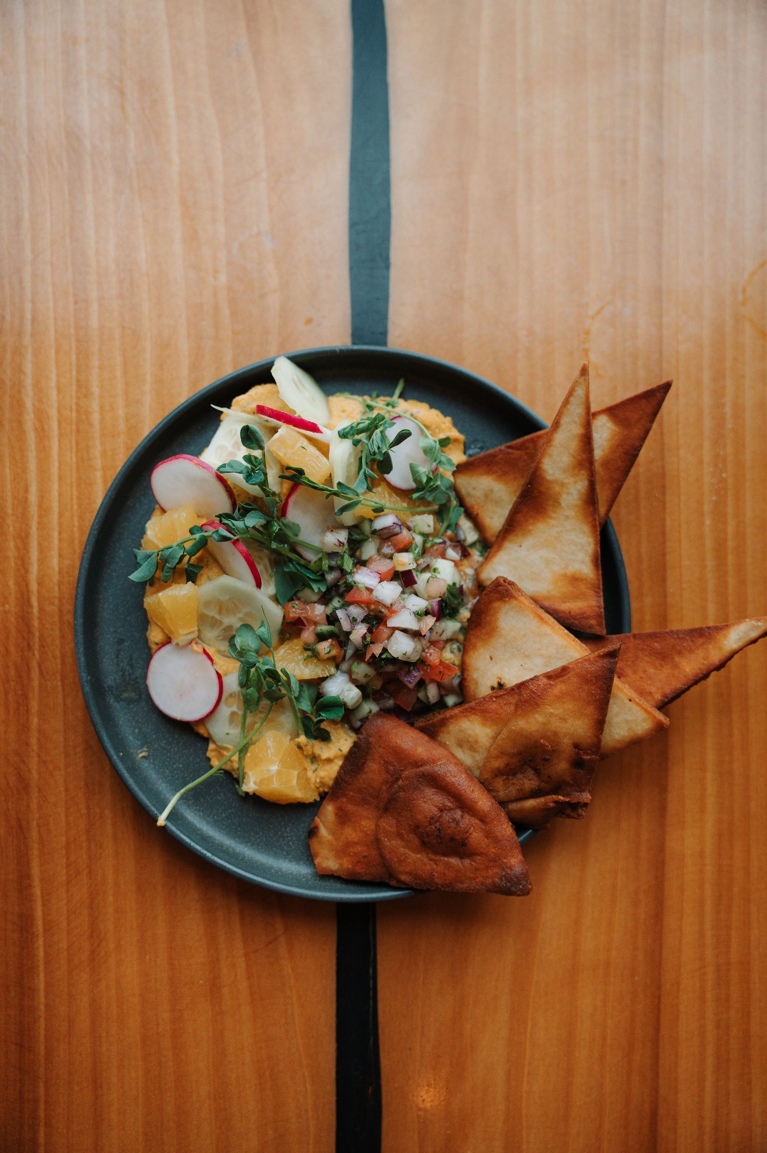 Overhead view of dark plate with fresh salad, radishes, pico de gallo, and golden fried wontons on wood table.