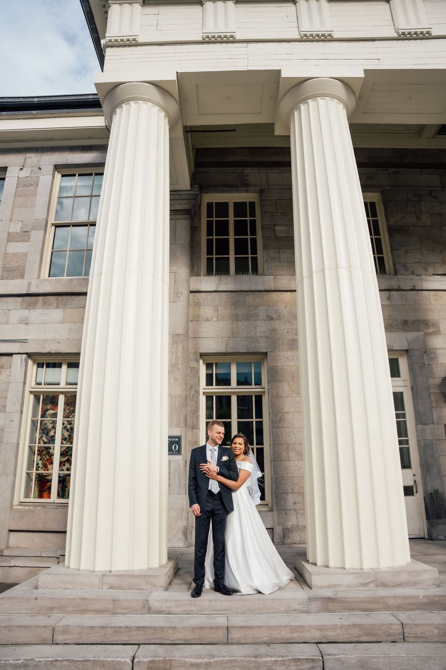 Wedding couple posing between grand white columns of a neoclassical building on their wedding day.