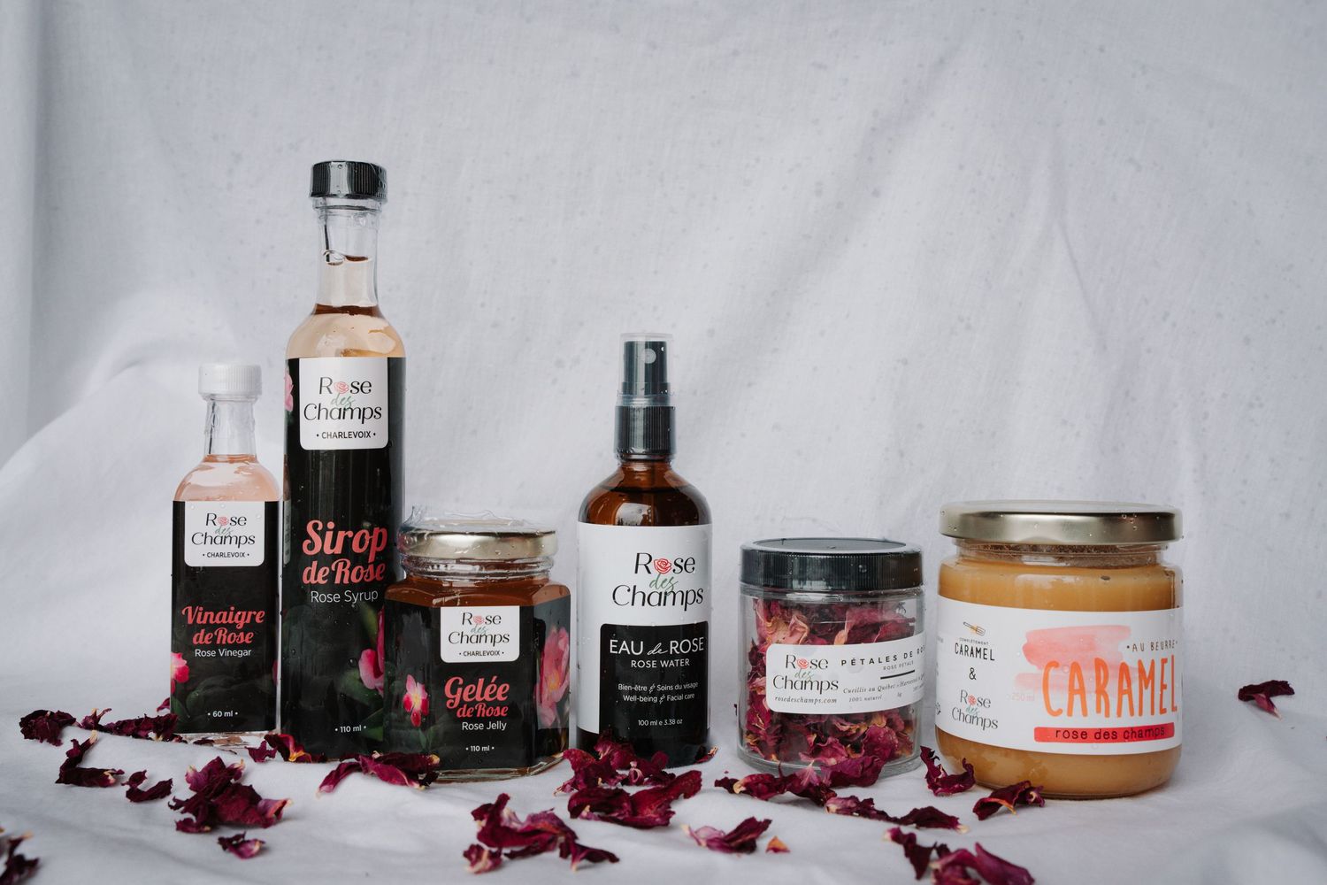 Collection of Rose des Champs artisan products including syrup, spray, and caramel on white cloth.