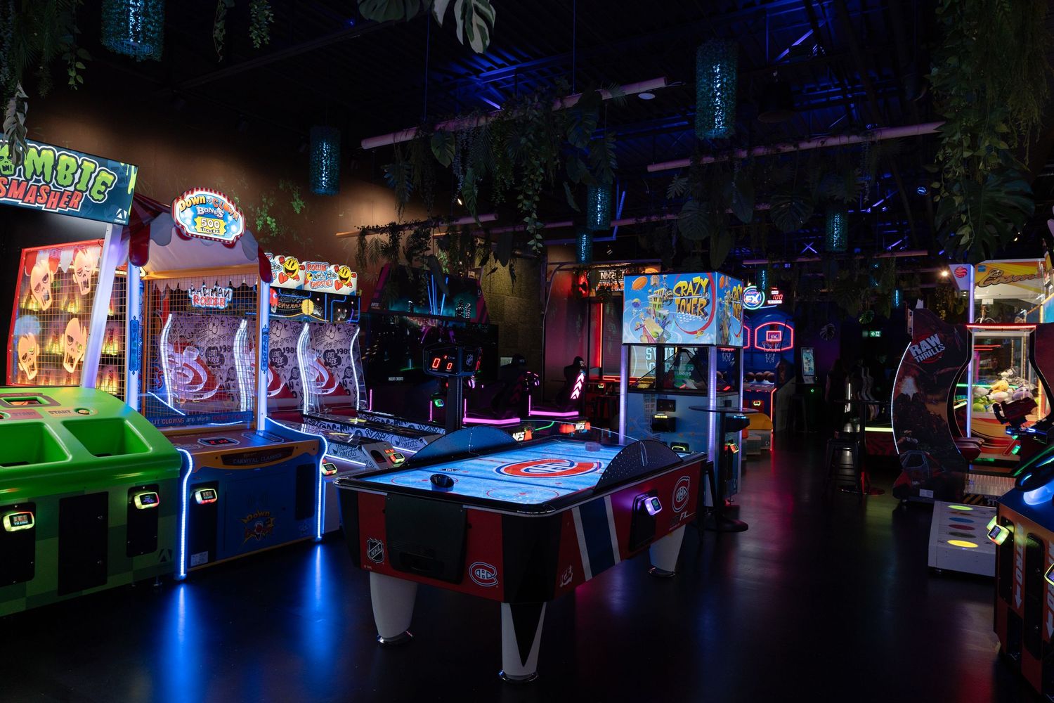 Empty neon-lit arcade room with multiple colorful arcade games and air hockey table.