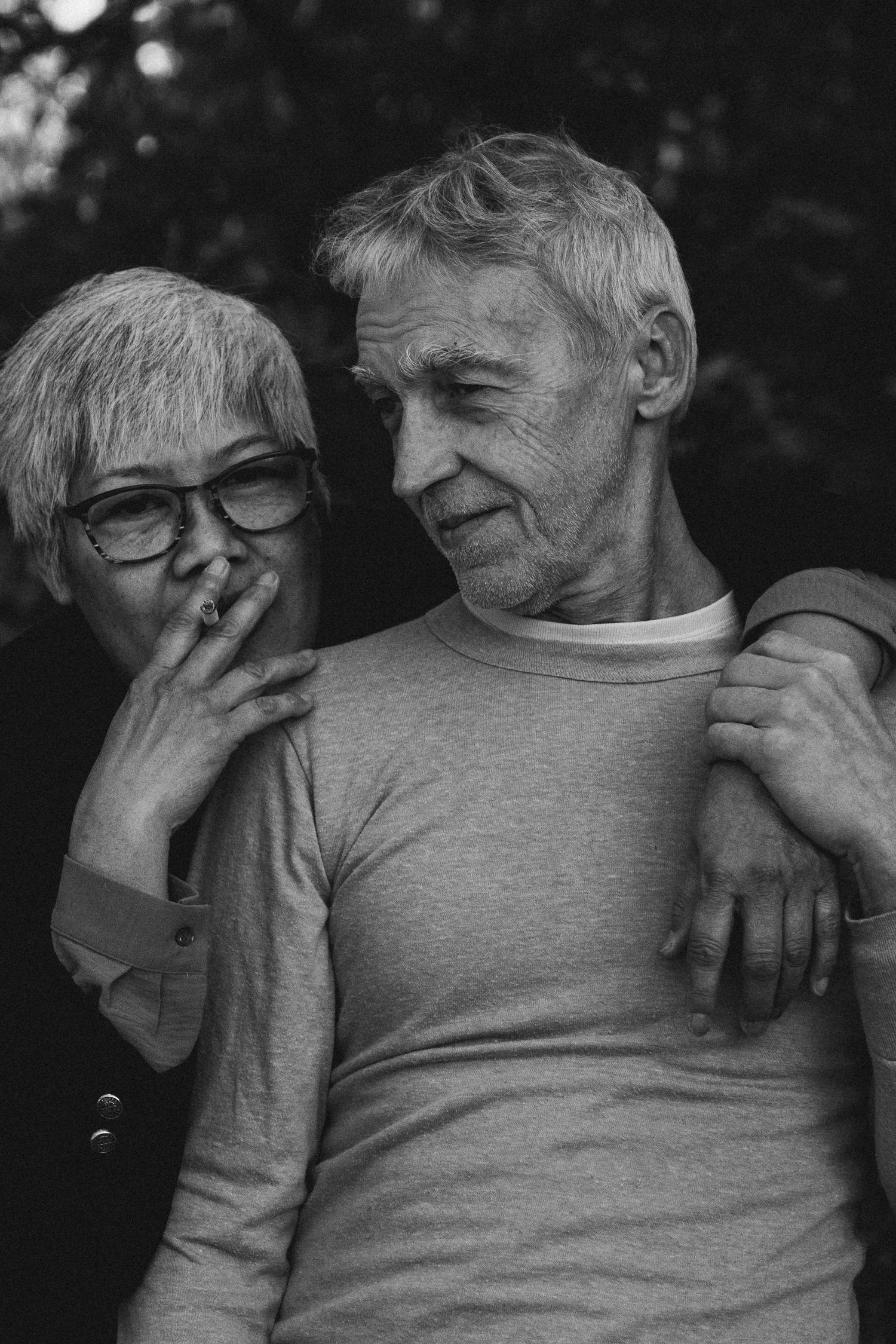 Black and white portrait of an elderly couple embracing outdoors, woman smoking a cigarette.