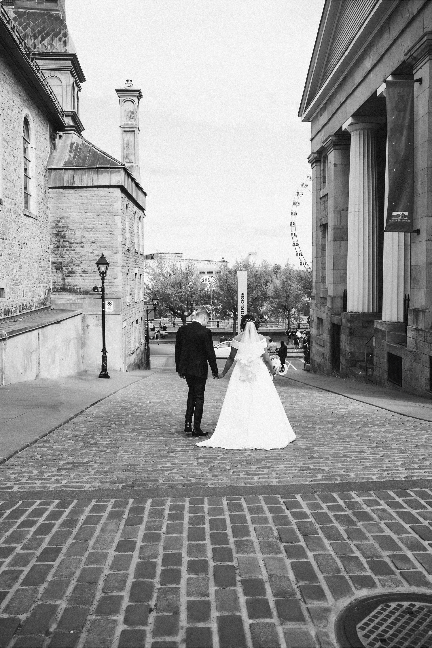 A bride and groom walk hand in hand along a cobblestone street in Montréal