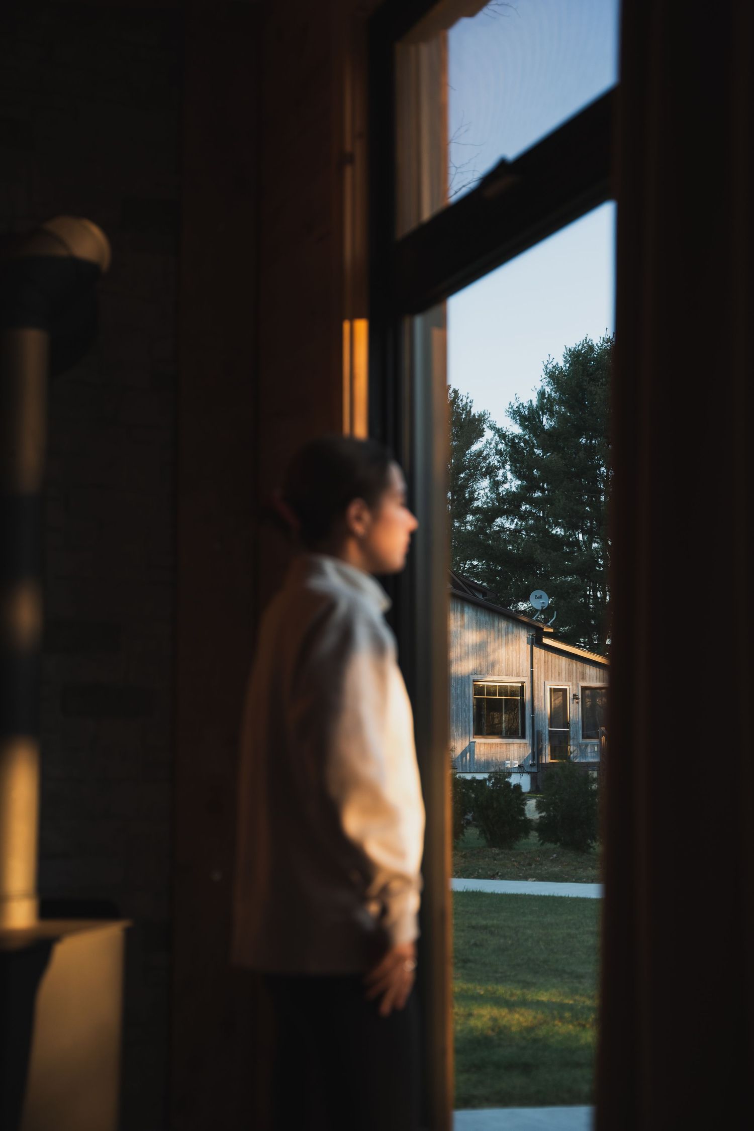 Young person standing by open door looking outside at golden hour light.