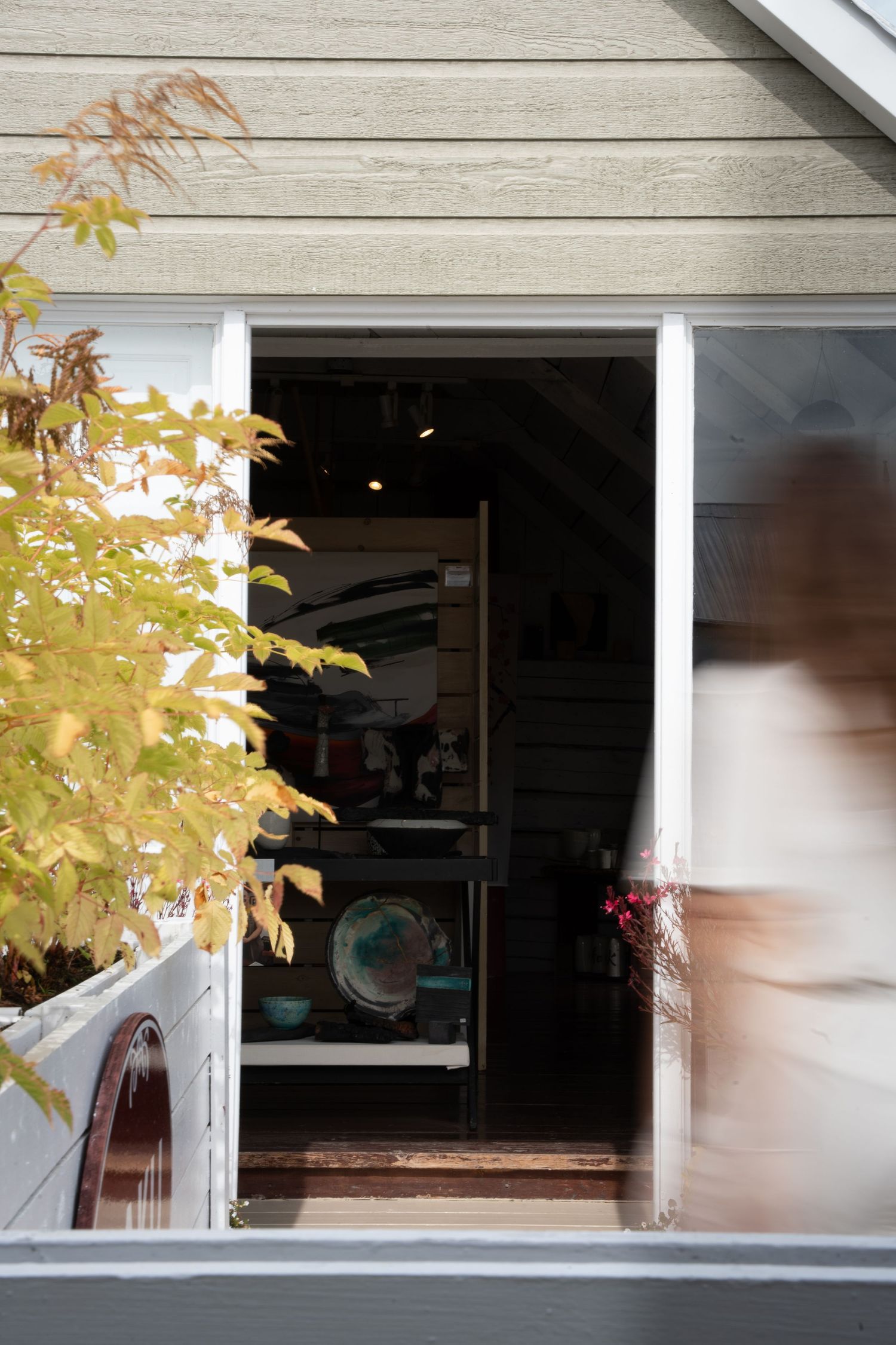 Open doorway of a wooden studio revealing shelves of colorful ceramic pottery inside.
