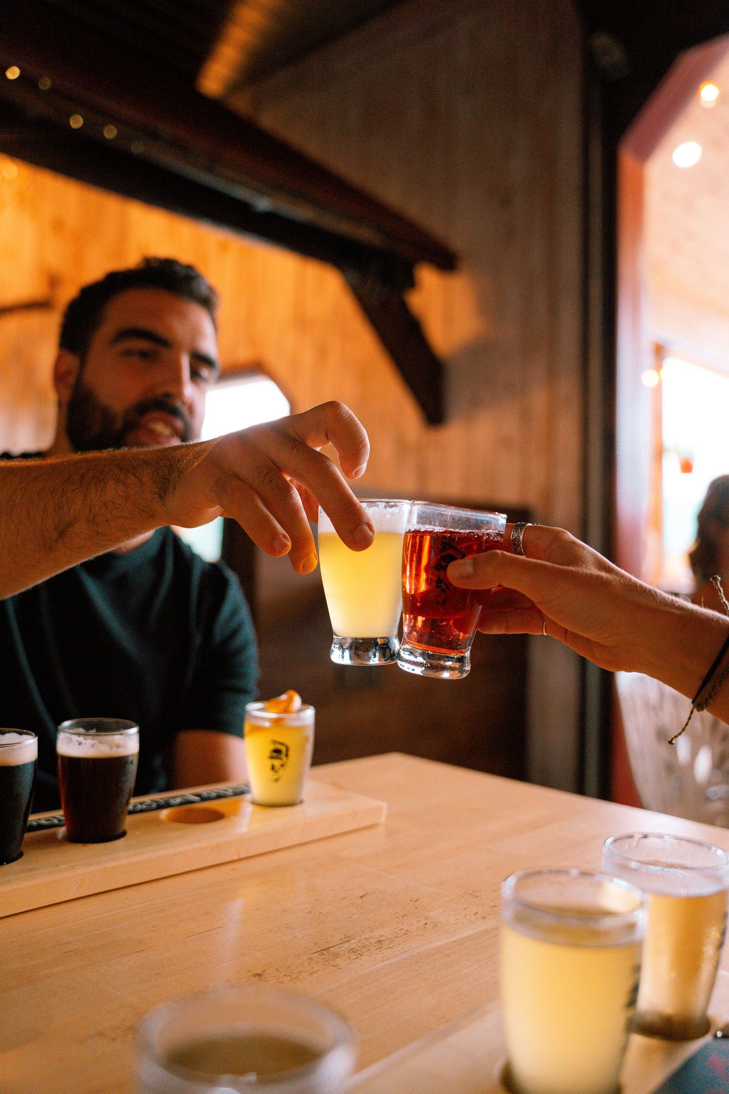 Bartender handing two small beer tasting glasses to a customer at a wooden brewery bar.