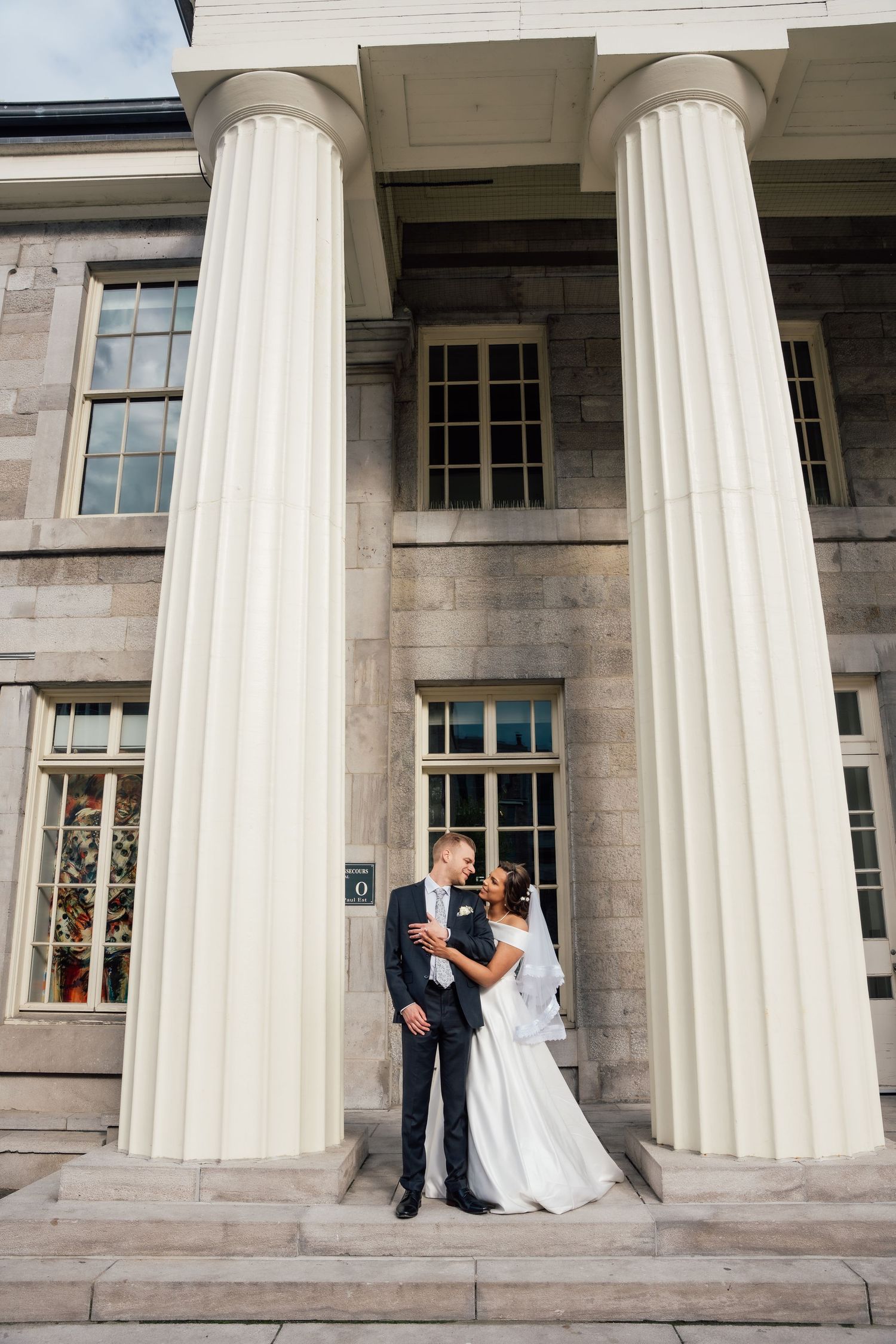 A bride and groom share a romantic moment on steps between grand white columns of a historic building.