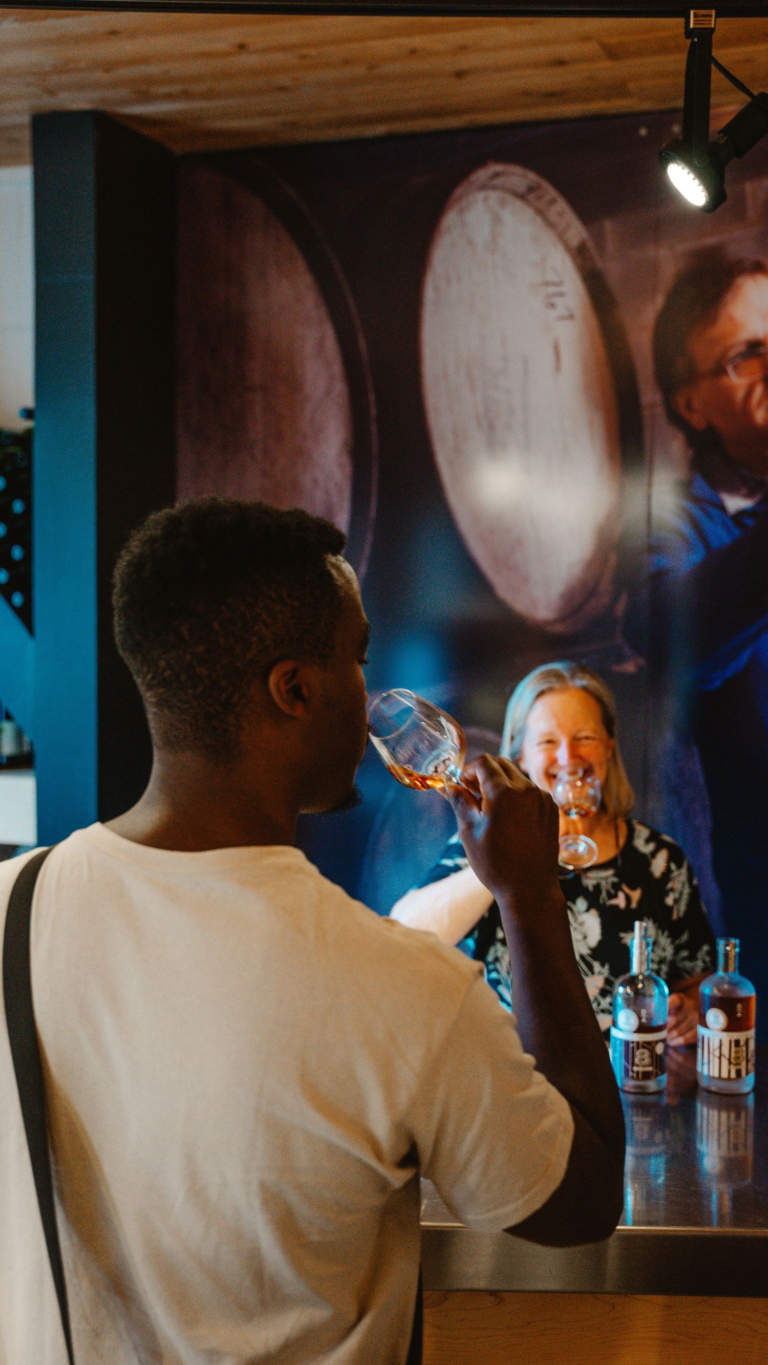 Man tasting whiskey at a distillery bar with barrels and bottles displayed in the background.